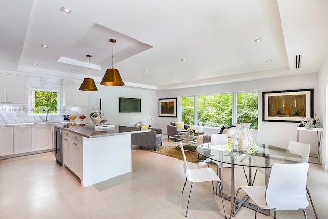 kitchen featuring tasteful backsplash, a tray ceiling, pendant lighting, dark stone countertops, and white cabinetry