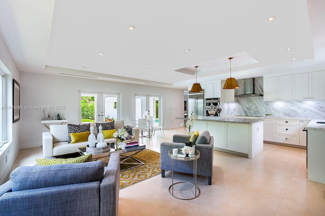 kitchen with white cabinets, a raised ceiling, wall chimney range hood, and stainless steel appliances