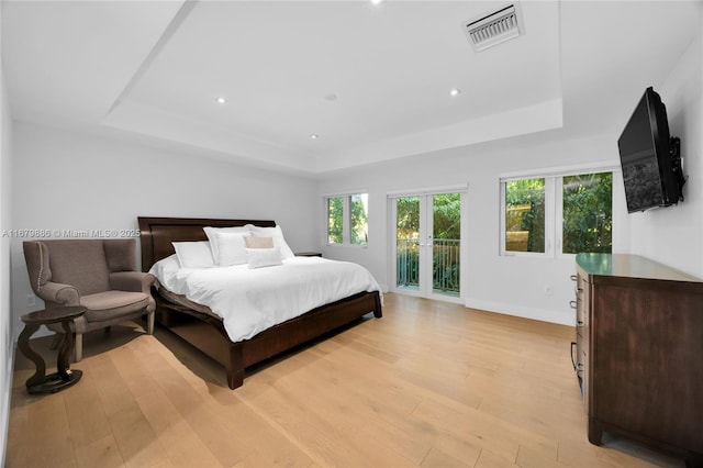 bedroom featuring access to outside, a raised ceiling, and light hardwood / wood-style floors