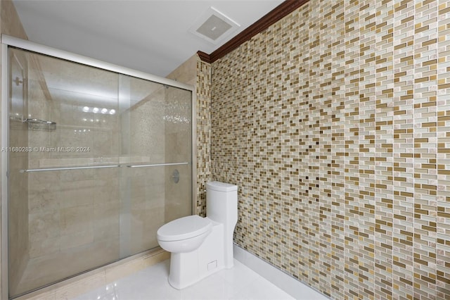 bathroom featuring tile patterned flooring, toilet, a shower with door, and tile walls