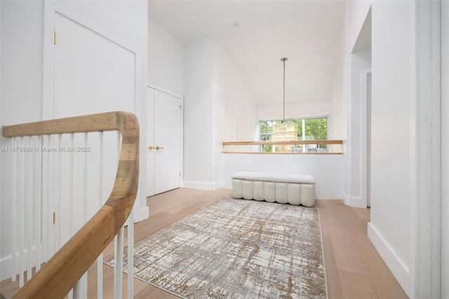 hall featuring light hardwood / wood-style floors, lofted ceiling, and an inviting chandelier