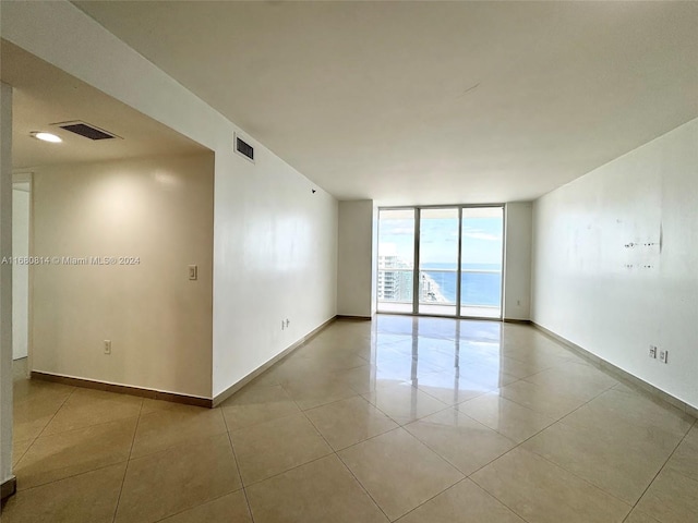 unfurnished room featuring a water view, light tile patterned flooring, and a wall of windows