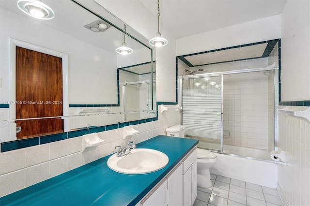 full bathroom with toilet, tile patterned flooring, tile walls, vanity, and combined bath / shower with glass door