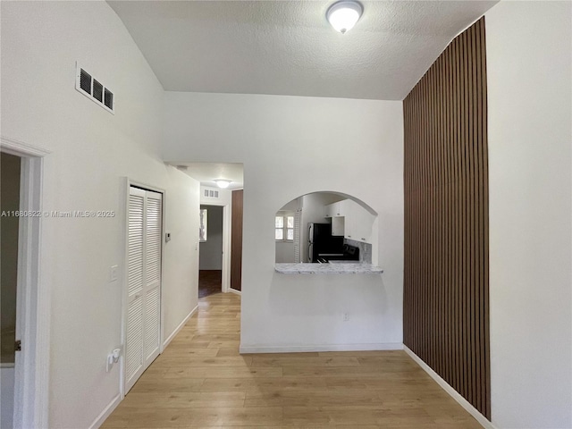 corridor with a textured ceiling and light hardwood / wood-style floors