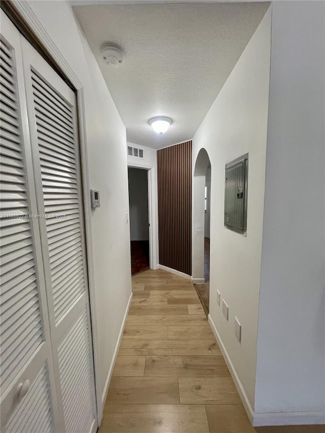 hallway with electric panel, light hardwood / wood-style floors, and a textured ceiling