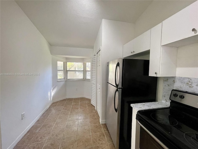 kitchen featuring stainless steel refrigerator, black range with electric stovetop, light tile patterned floors, light stone counters, and white cabinets