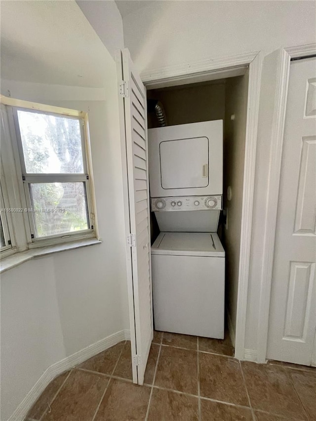 laundry room featuring dark tile patterned floors and stacked washer / drying machine