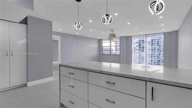 interior space featuring white cabinetry, light stone counters, and pendant lighting