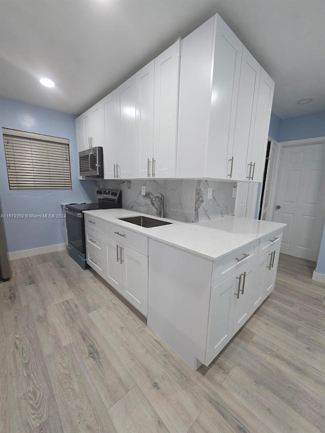 kitchen with decorative backsplash, white cabinets, electric range, light hardwood / wood-style floors, and sink