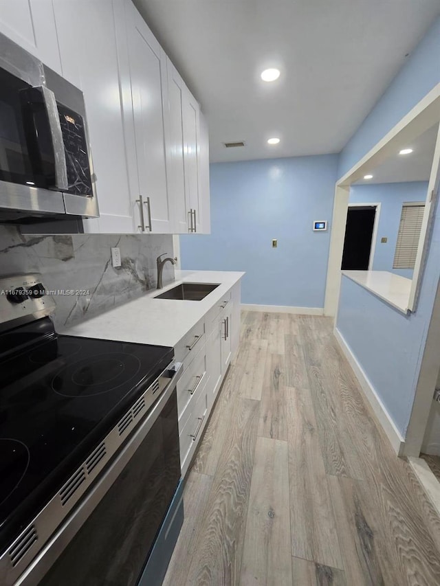 kitchen with decorative backsplash, light hardwood / wood-style flooring, sink, white cabinetry, and appliances with stainless steel finishes