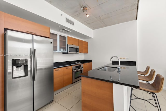 kitchen featuring kitchen peninsula, appliances with stainless steel finishes, a kitchen breakfast bar, light tile patterned flooring, and sink