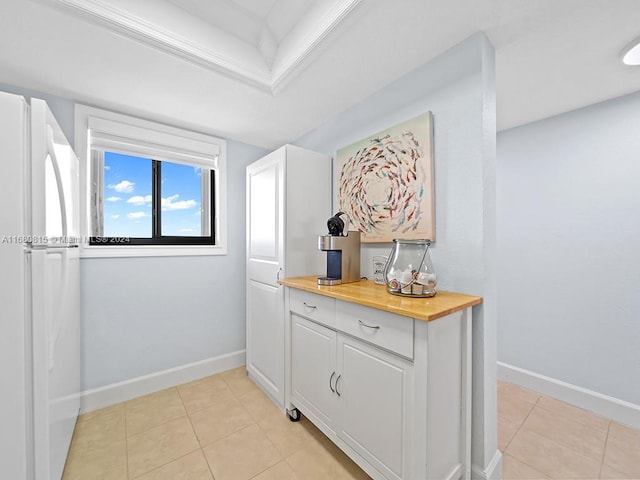 interior space featuring wood counters, light tile patterned floors, white fridge, and white cabinets