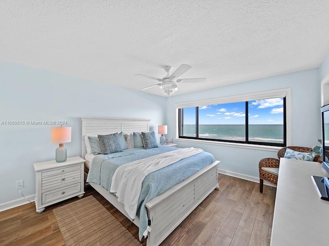 bedroom with hardwood / wood-style floors, a textured ceiling, a water view, and ceiling fan