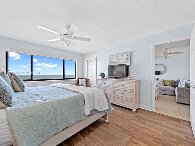 bedroom with ceiling fan, light hardwood / wood-style floors, and a textured ceiling