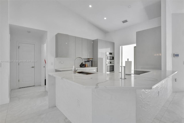 kitchen featuring kitchen peninsula, light stone countertops, vaulted ceiling, gray cabinets, and sink