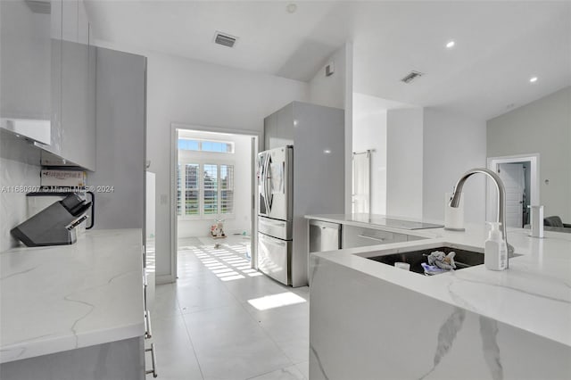 kitchen with white cabinets, light stone countertops, vaulted ceiling, stainless steel refrigerator, and sink