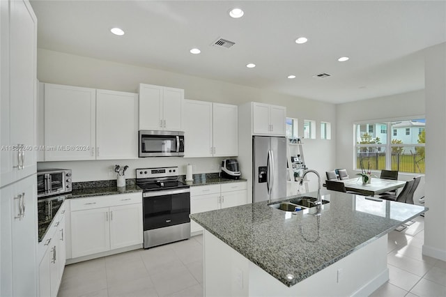 kitchen featuring white cabinetry, sink, stainless steel appliances, dark stone countertops, and a center island with sink