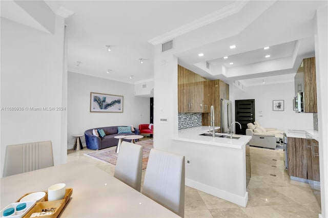 kitchen with tasteful backsplash, appliances with stainless steel finishes, a raised ceiling, kitchen peninsula, and crown molding