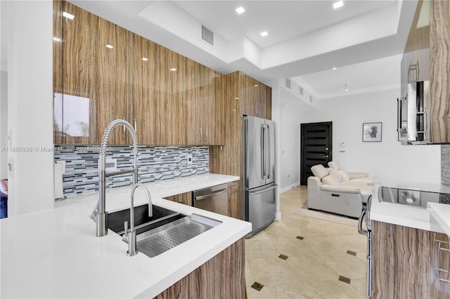 kitchen with tasteful backsplash, sink, a tray ceiling, stainless steel appliances, and light tile patterned floors