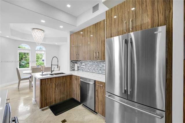 kitchen featuring kitchen peninsula, tasteful backsplash, a raised ceiling, appliances with stainless steel finishes, and sink