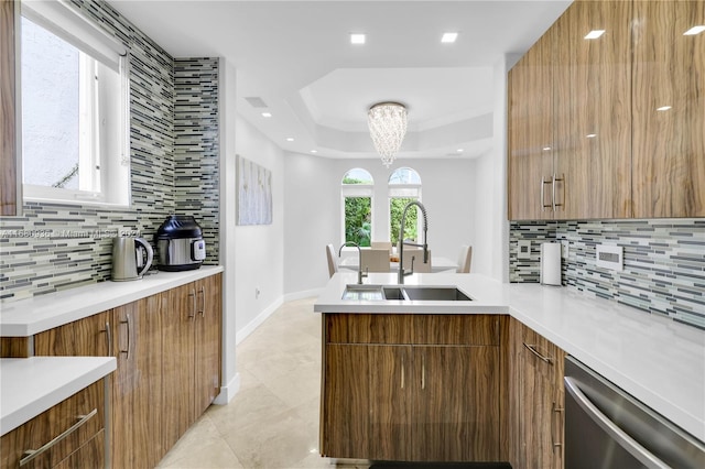 kitchen featuring dishwasher, backsplash, sink, a raised ceiling, and a chandelier