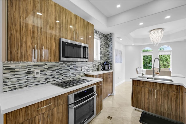 kitchen featuring a tray ceiling, backsplash, sink, a chandelier, and appliances with stainless steel finishes