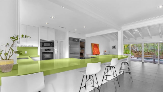 kitchen featuring kitchen peninsula, white cabinetry, a kitchen bar, vaulted ceiling with beams, and built in appliances