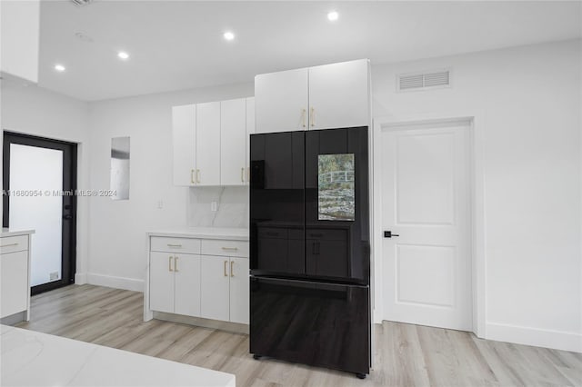 kitchen featuring black refrigerator, decorative backsplash, white cabinets, and light hardwood / wood-style flooring