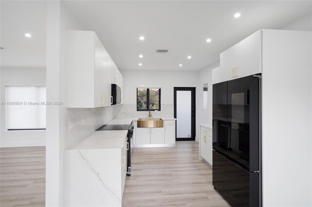 kitchen featuring light hardwood / wood-style floors, black fridge, white cabinetry, and range