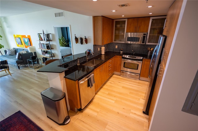 kitchen with appliances with stainless steel finishes, sink, light wood-type flooring, and decorative backsplash