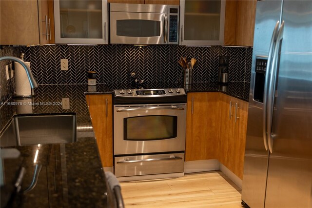 kitchen with appliances with stainless steel finishes, light hardwood / wood-style flooring, and dark stone counters