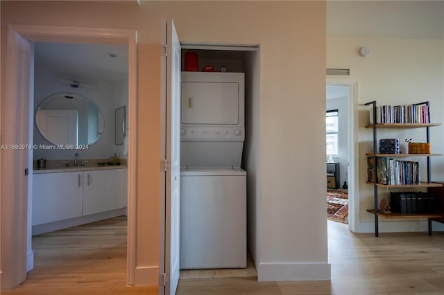 clothes washing area with light hardwood / wood-style floors, stacked washing maching and dryer, and sink