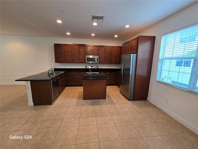 kitchen with light tile patterned floors, sink, appliances with stainless steel finishes, and a center island with sink