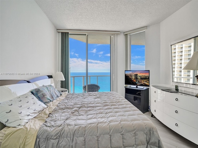 bedroom featuring hardwood / wood-style floors, a textured ceiling, access to outside, and expansive windows