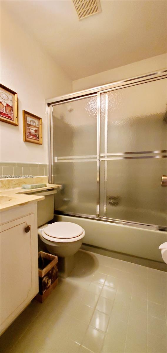 full bathroom with vanity, tile patterned floors, combined bath / shower with glass door, and toilet