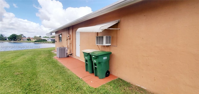 view of side of home with central air condition unit, a lawn, a wall mounted air conditioner, and a water view