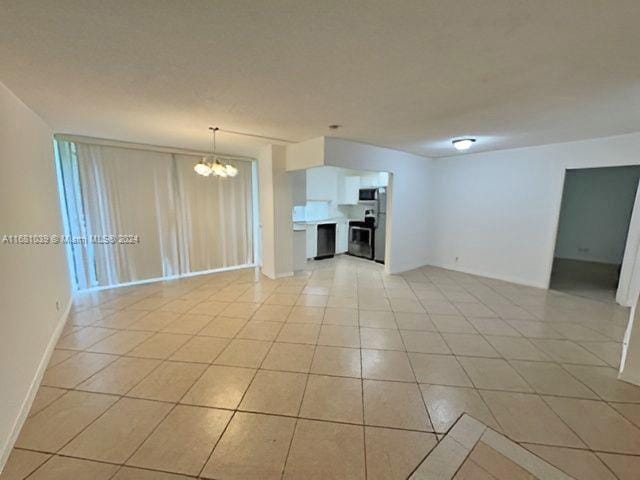 unfurnished room featuring light tile patterned floors, a chandelier, a fireplace, and baseboards