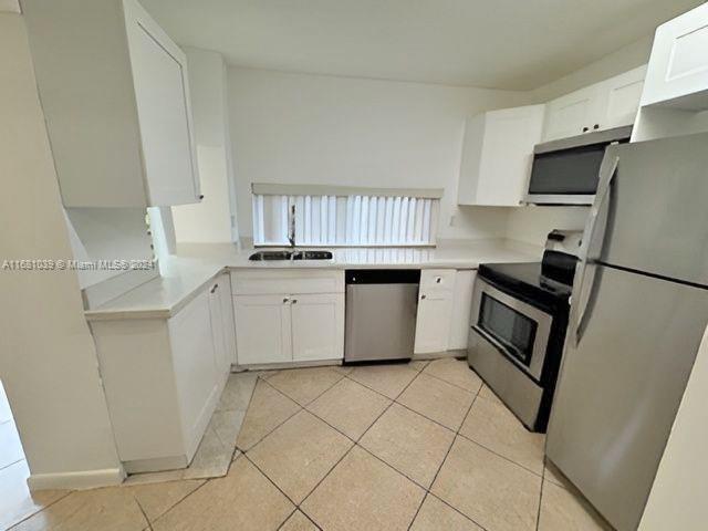 kitchen featuring light tile patterned floors, a sink, white cabinetry, light countertops, and appliances with stainless steel finishes