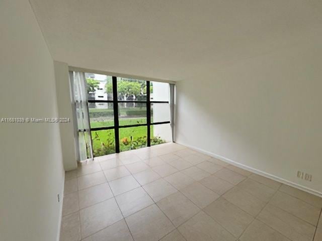 empty room with floor to ceiling windows, tile patterned flooring, and baseboards
