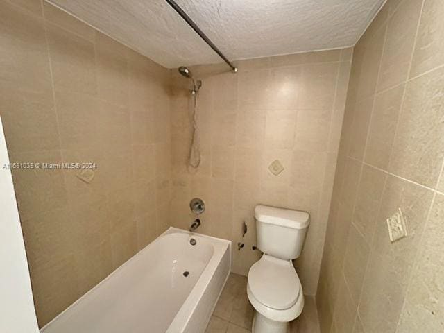 bathroom featuring toilet, tile patterned flooring, tiled shower / bath, tile walls, and a textured ceiling