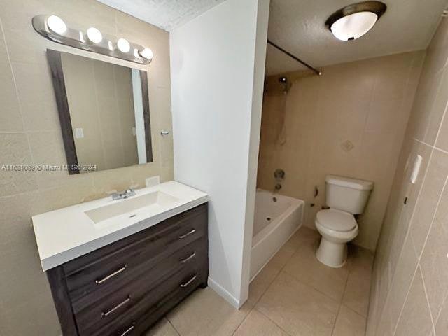 full bathroom with toilet, tile patterned flooring, shower / bathing tub combination, vanity, and tile walls