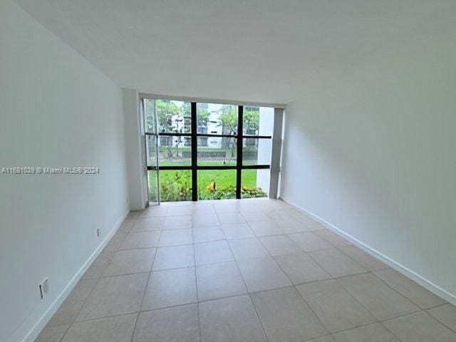 unfurnished room with a wall of windows, baseboards, and light tile patterned floors