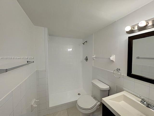 bathroom featuring toilet, vanity, a tile shower, and tile walls