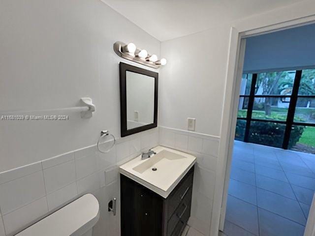 half bath featuring tile walls, vanity, and a wainscoted wall