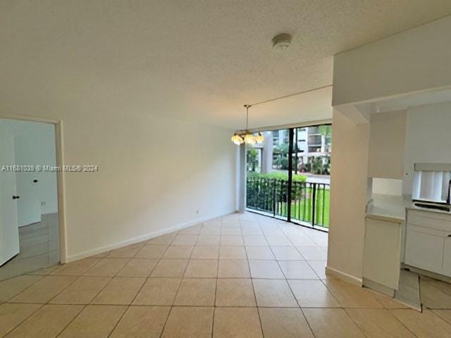 empty room featuring a notable chandelier, a textured ceiling, and light tile patterned floors