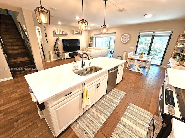 kitchen featuring dark wood-type flooring, an island with sink, sink, decorative light fixtures, and stainless steel dishwasher