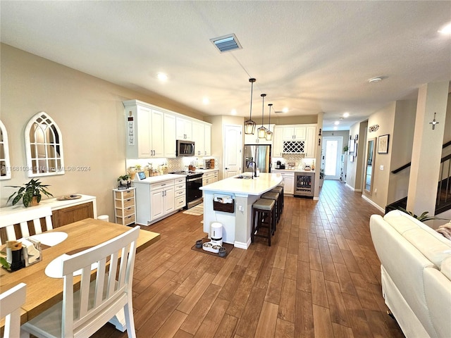 kitchen with a kitchen breakfast bar, an island with sink, white cabinetry, appliances with stainless steel finishes, and dark hardwood / wood-style flooring