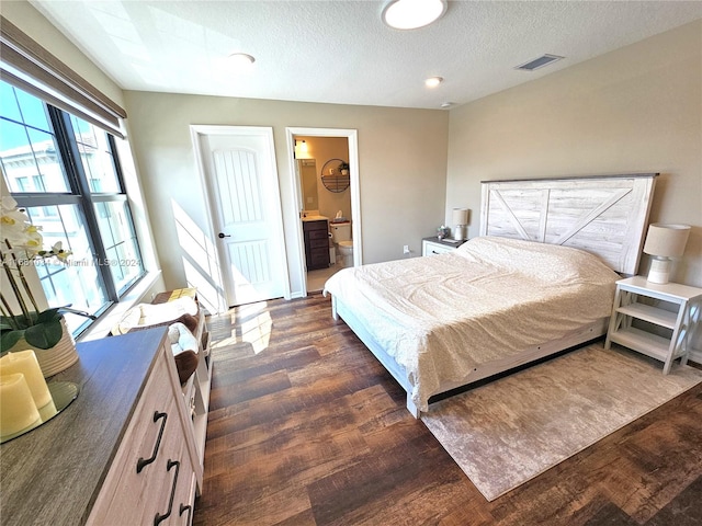 bedroom with ensuite bathroom, a textured ceiling, and dark hardwood / wood-style floors