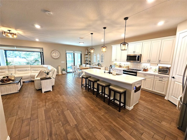 kitchen featuring appliances with stainless steel finishes, an island with sink, hanging light fixtures, a kitchen breakfast bar, and white cabinets