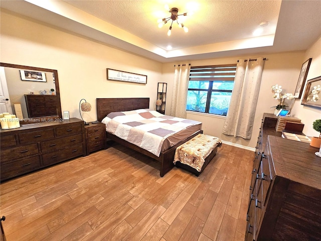 bedroom featuring light hardwood / wood-style floors, a raised ceiling, and a textured ceiling